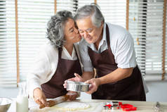 亚洲祖母亲吻祖父, 而他们烤饼干在家里。浪漫, 恋爱中的情侣.