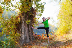 美丽健康的女人伸展她的腿和手臂准备早晨跑在秋天的森林与五颜六色的树木和河流.