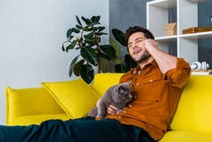 欢快的人在智能手机上与灰色的猫沙发上交谈