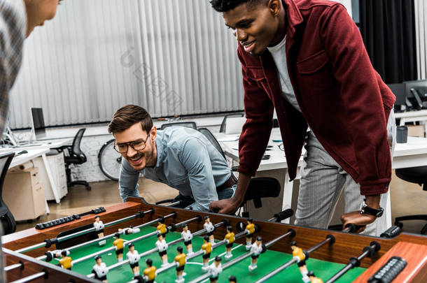 微笑的多元文化商人在办公室玩桌上足球