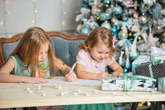 孩子们的小女孩姐妹们带着礼物快乐时尚美丽的圣诞室内给圣诞老人写了一封信