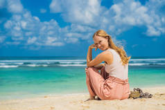 年轻的妇女坐在沙滩上, 欣赏绿松石水在惊人的梅拉斯蒂海滩, 巴厘岛, 印度尼西亚.