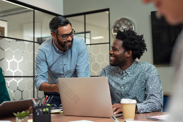 两个随意的商业伙伴坐在一起工作的肖像。一群创意商人在现代办公室工作。英俊的成熟商人与非洲人讨论事务, 并在一个<strong>会议室</strong>里一起微笑.