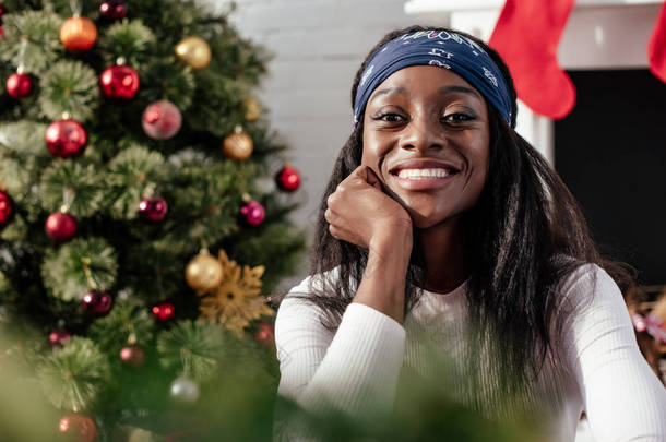 微笑迷人的非洲裔美国妇女的肖像在家里看相机, 圣诞节概念