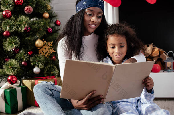 微笑的非洲裔美国母亲和女儿阅读书籍在家里, <strong>圣诞</strong>节概念