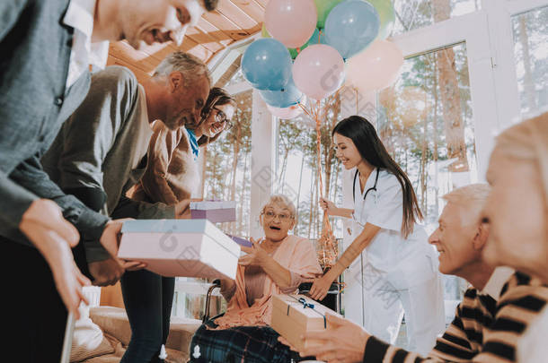 礼物。轮椅。疯狂快乐退休的人。生日派对庆祝。<strong>气球</strong>。客人。年轻人和老人。疗养院。祝贺。老年妇女。送礼。太惊讶了非常开心.