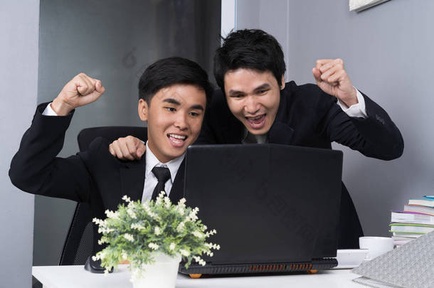 快乐的两个商人用笔记本电脑成功地实施了一项工作计划