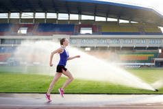 运动。运动年轻女子在粉红色运动鞋跑附近的洒水车在跑的跑道体育场。概念运行
