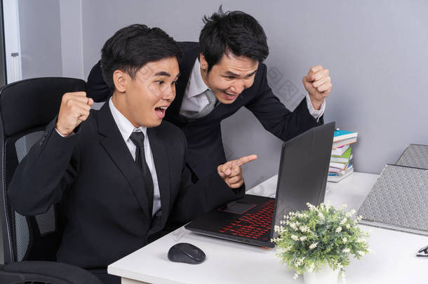 快乐的两个商人用笔记本电脑成功地<strong>实施</strong>了一项工作计划