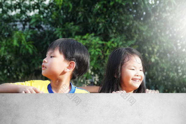 一个快乐的亚洲男孩和女孩的肖像偷看在水泥围栏。一个小孩子的微笑, 弟弟和妹妹在阳光明媚的夏日度过一段时间。家庭, 孩子, <strong>兄弟</strong>姐妹, 周末概念.                            