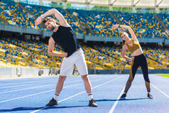 年轻的运动夫妇做侧弯前训练体育场馆跑道
