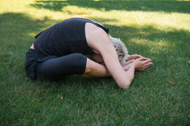 妇女在公园草地上练习瑜伽的侧面观