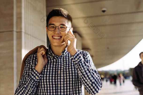 年轻的亚洲男人微笑着在城市里<strong>漫步</strong>, 在电话和微笑中交谈