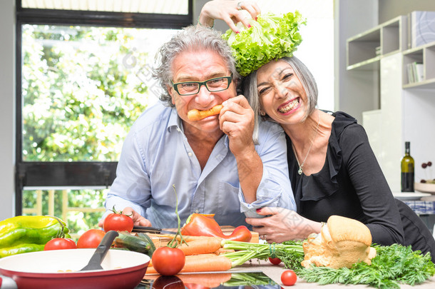 年长的夫妇在厨房与健康食品-退休的人与男人和女人准备午饭与生物蔬菜烹饪到家里吃饭-快乐老人概念与成熟有趣的养老金领取者开心