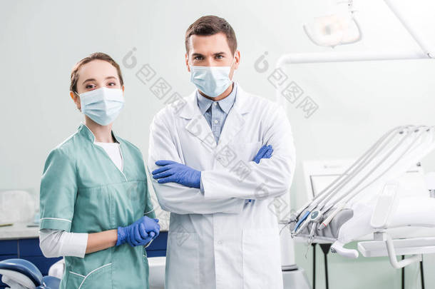 戴口罩的牙医在牙科诊所与交叉的手臂站立