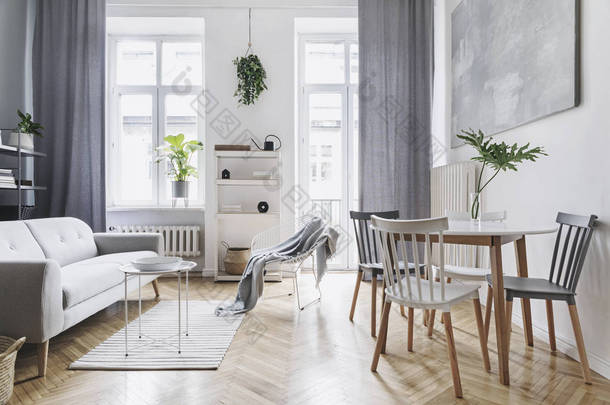 明亮的家庭北欧客厅与设计式的桌子，家庭表，植物，<strong>白色</strong>书架在墙上。棕色木制镶木地板。白墙上的抽象绘画。简约<strong>内饰</strong>的概念.