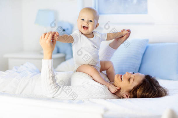 母亲和孩子在一张白色的床上。<strong>妈妈</strong>和宝宝尿布在阳光明媚的卧室里玩的男孩。父母和小孩在家中休息。让大家一起开心的家庭。床上用品和婴儿苗圃纺织.