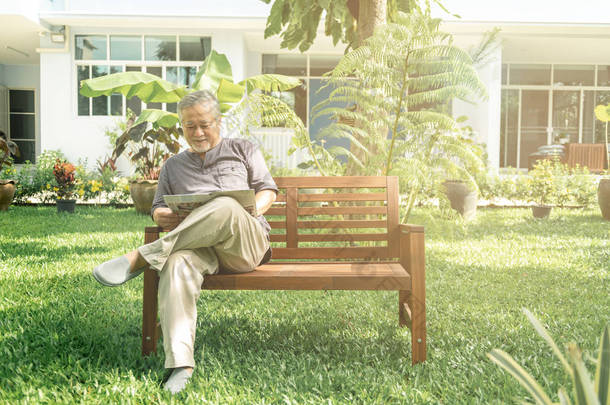 老人坐在花园看报的长凳上。亚洲资深男士, 资深生活方式概念.