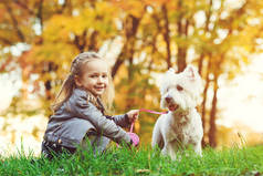 秋天公园里有狗的小女孩。可爱的微笑的女孩与她的宠物散步乐趣。快乐的孩子与狗在户外休息。秋天。快乐童年