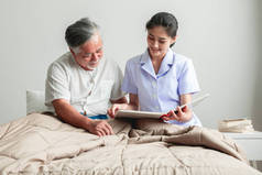 年轻漂亮的女护士读书给老人。亚洲妇女读书给老亚洲人在床上留白胡子.