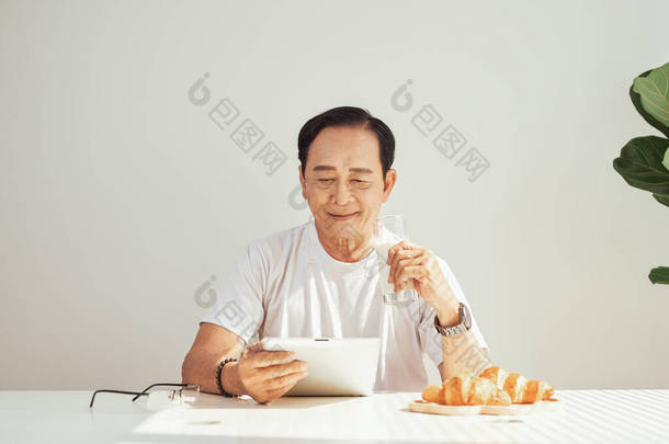 老人喝牛奶和阅读新闻在他的数字平板电脑，而不是报纸