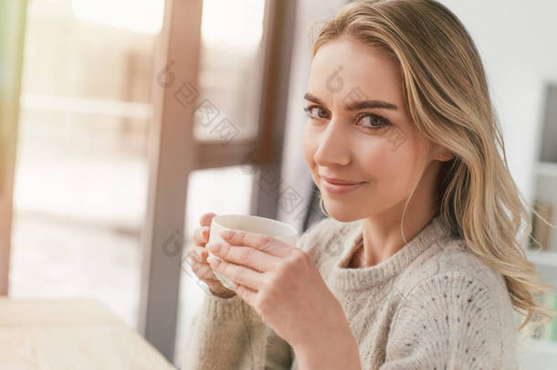 快乐的女人拿着杯子与茶, 看着相机在家里