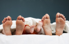 在床上的幸福家庭的一对腿- -父母和婴儿