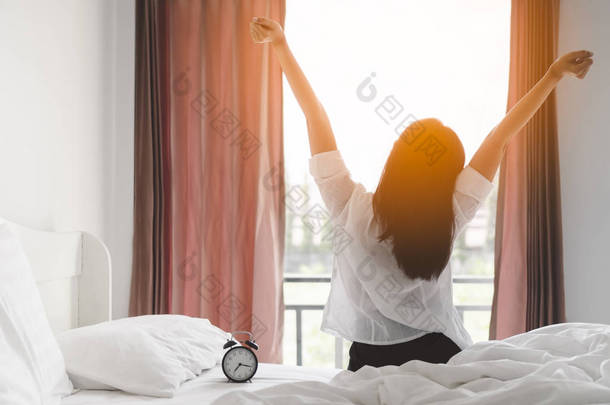 快乐的亚洲<strong>妇女</strong>在床上起床后, 早上醒来后, 在卧室阳光照耀通过窗帘