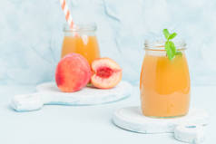 桃冰沙在玻璃罐子与新鲜成熟的果子和绿色薄荷叶子在蓝色柔和的背景-原始的甜甜点或早餐饮料为健康有机饮食概念.