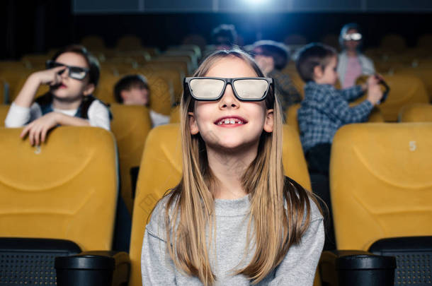 选择焦点可爱的微笑的孩子在3d 眼镜坐与朋友坐在电影院