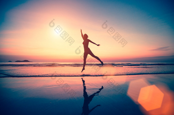 在日落时在沙滩上跳跃的女人.
