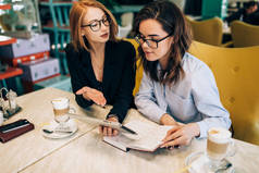 两个女孩在一家咖啡厅的商务会议上。喝咖啡。讨论未来的公司及其项目。签订合同。红头发的女孩和褐发女郎.