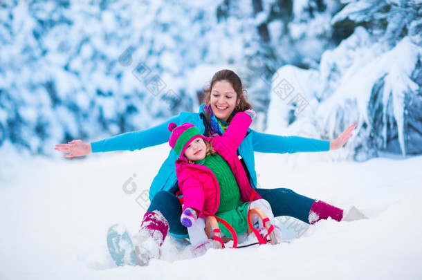 母亲和儿童雪橇在雪的公园