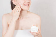 女孩在用白毛巾洗澡后, 把一罐奶油放在脸上。手的特写。概念美容护肤