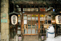 日本北海道小樽, 2018年2月14日: 复古和古老的日本餐厅在下雪的冬天雪人娃娃的前面。小樽在冬季被命名为爱的城市和情侣的目的地.