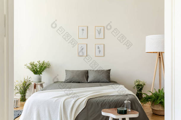 一个生态友好的粉彩卧室<strong>内饰</strong>与灰色亚麻和枕头和香草毯在一张双人床上。一束野花在花瓶周围的床上。墙上的自然插图。真实照片