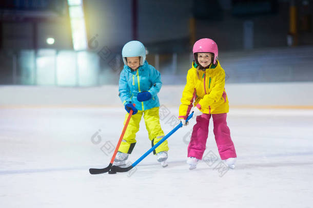 孩子们在室内溜冰场玩冰球。孩子们的健康冬季运动。男孩和女孩用曲棍球棍打冰球。儿童滑冰。小男孩放学后参加体育训练。雪和冰乐趣.