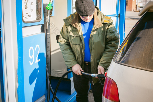 男子在一个<strong>加油站</strong>填充车辆油箱燃料。成年男子与一个小胡子和眼镜，加油前长途旅行的道路上向非网络<strong>加油站</strong>汽车
