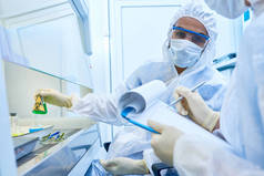 两名科学家在医学研究实验室中佩戴防护服和口罩的画像
