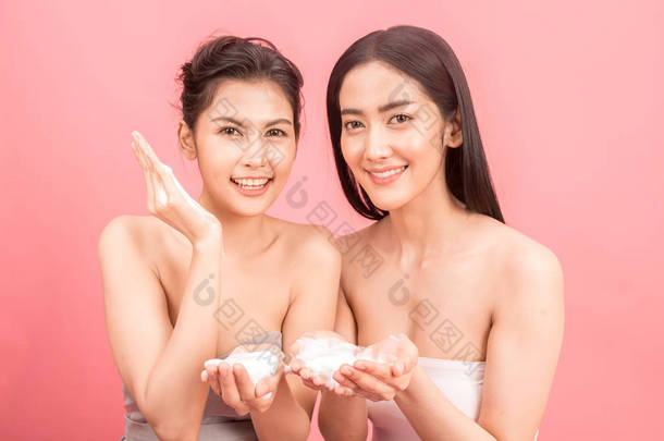 两个美丽的女人的肖像举行洗脸的形式. 美容水疗. 粉红色背景上的完美新鲜肌肤