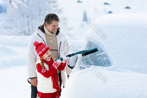 父亲和孩子在暴风雨后刷洗和铲去汽车上的雪.带着冬刷和<strong>刮胡刀</strong>的父母和孩子在一夜暴风雪之后清扫了家里的汽车。山里的圣诞假期.