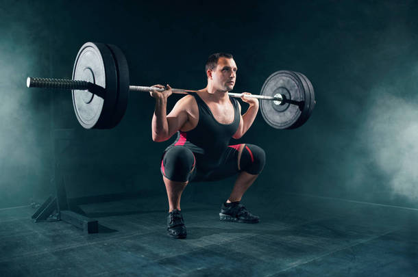 运动服装的强力举重运动员在健身房里和杠铃蹲着。举重锻炼, 举重训练, 举重运动员在运动俱乐部的重量工作