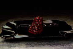 成熟的石榴在一个黑色的盘子。热带水果。玻璃上的反射。多汁的红粒.