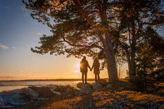 冬季日落时, 在爱沙尼亚南部的佩普西湖岸边, 年轻夫妇手牵手站在松树下