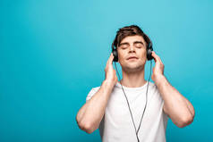 梦幻般的年轻人在耳机听音乐与蓝色背景闭上眼睛