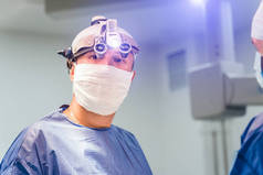 使用医疗设备进行外科手术的过程。 手术室里的外科医生，带着手术器械。 医疗背景。 医生戴口罩和双目手术眼镜的情况.
