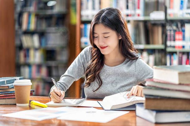 亚洲青年学生穿着休闲服在大学图书馆阅读和做作业，或与<strong>各种</strong>书籍和固定在书架背景的木桌上，回到学校