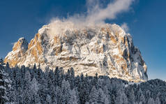 在阳光明媚的冬日，意大利阿尔卑斯山的冰雪覆盖着树木和高山，背景为雪