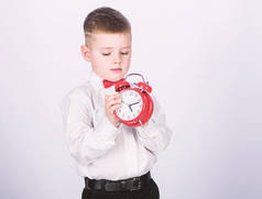 设置闹钟。小男孩拿着红钟。是时候了时间表和时间。早上例行公事。带闹钟的小学生。孩子可爱的男孩白衬衫红色领结。发展自律