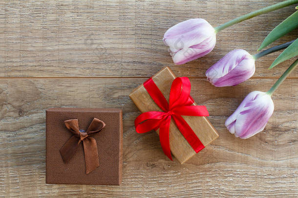 有彩带和美丽的丁香郁金香在木板上的礼品盒。顶部视图。假日送礼的概念.